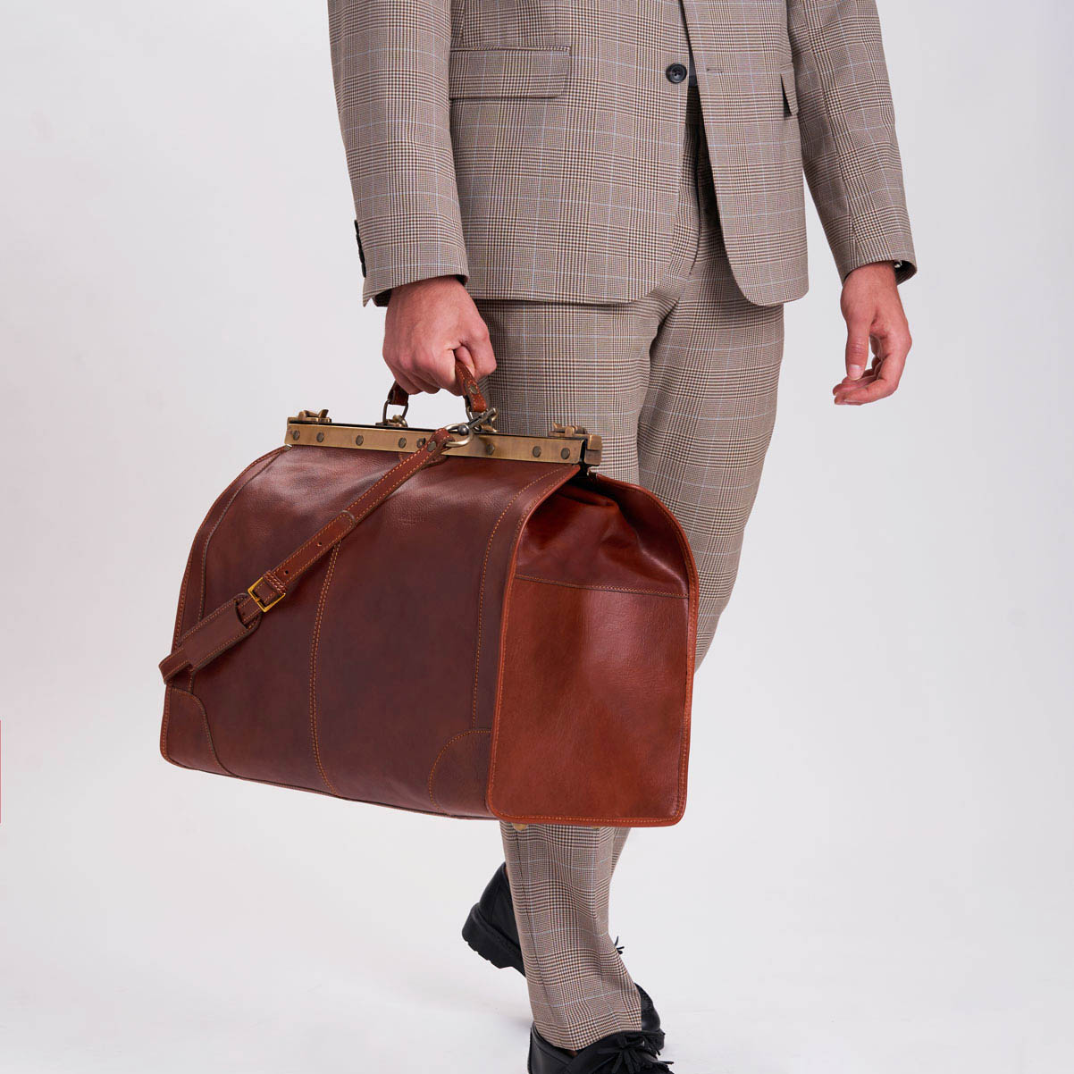 Braune Ledertasche mit messing optik Schnalle von Fantini Pelletteria jetzt zu haben auf Herr&Gut ein Mann mit Anzug trägt die Tasche im Artztaschenoptik ist aber eine Reise Tasche, bekannt auch als Weekender